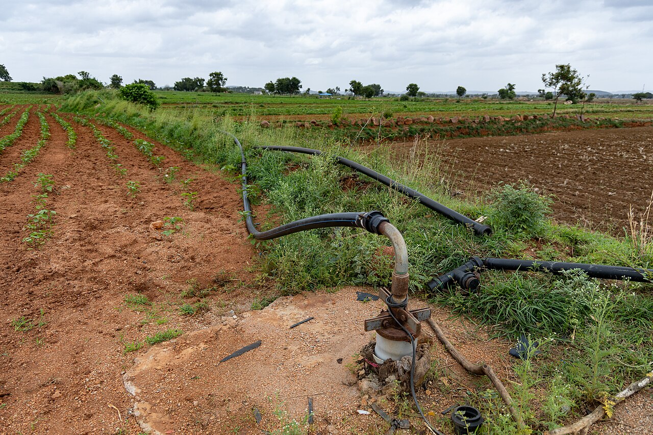 Pompa su pozzo perforato (pozzo artesiano) con distribuzione tubazioni per l'irrigazione in un appezzamento agricolo